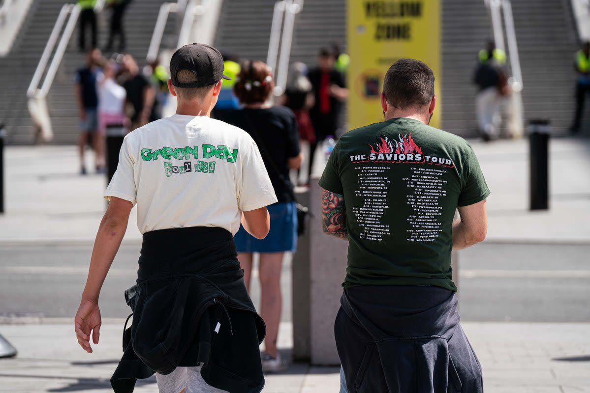 A photo taken of two Green Day wearing tour t-shirts as they walk towards the stadium
